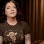 Ashley McBryde, seen in a past interview setting, opens up about her recent vocal cord injury that will keep her silent for days while she works to keep her tour dates on track.
