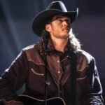 A young Blake Shelton in a cowboy hat plays guitar on stage, recalling how songwriter Mae Boren Axton inspired him to move to Nashville at 17.